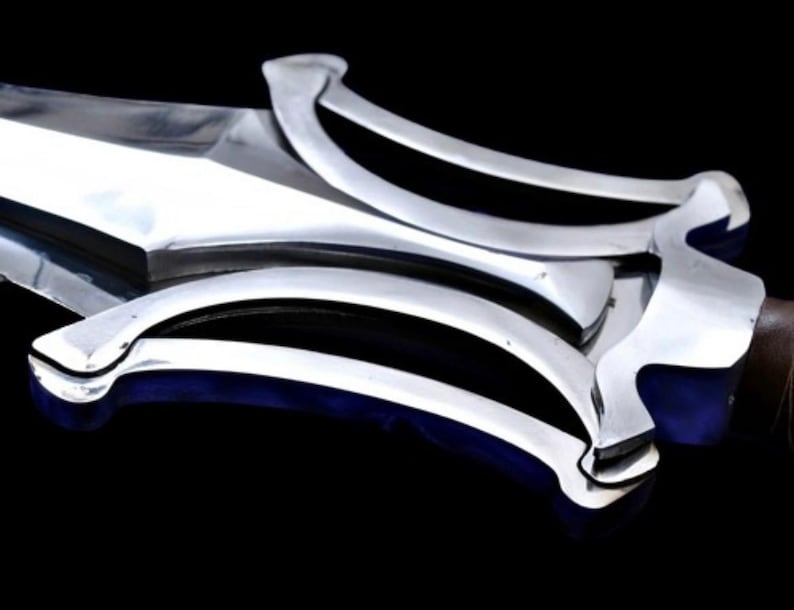 May include: Close-up of a polished silver sword with a wide blade and ornate, curved handguard. The handguard features a series of parallel black lines. The sword's handle is a dark brown color. The background is black.