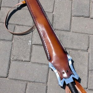 Pu&ograve; includere: Un fodero per spada in pelle marrone con un'elsa decorativa argentata e blu. Il fodero &egrave; cucito lungo i bordi e ha un cinturino per il trasporto. L'impugnatura della spada &egrave; avvolta in pelle nera.