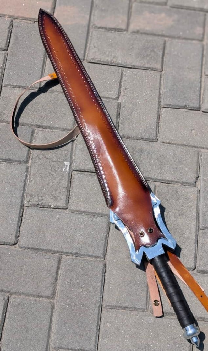 Pu&ograve; includere: Un fodero per spada in pelle marrone con un'elsa decorativa argentata e blu. Il fodero &egrave; cucito lungo i bordi e ha un cinturino per il trasporto. L'impugnatura della spada &egrave; avvolta in pelle nera.