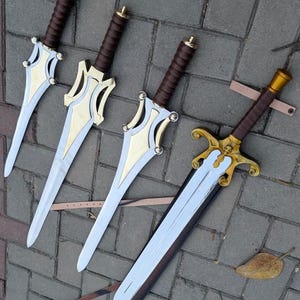 May include: Four fantasy swords with silver blades, gold accents, and brown wrapped handles. The swords are arranged on a gray brick surface. One sword has a skull design on the hilt and a leather sheath.