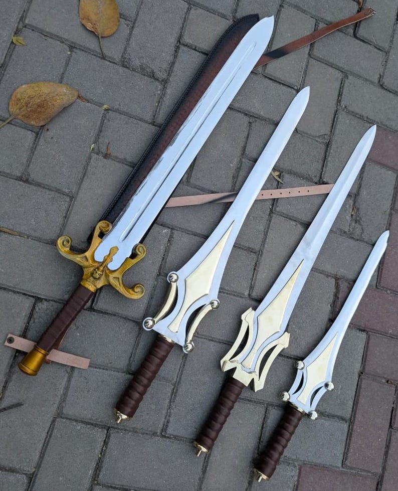 May include: Four fantasy swords with silver blades and ornate gold and brown handles. The largest sword has a brown leather sheath. The swords are arranged diagonally on a gray brick surface.
