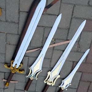 May include: Four fantasy swords with silver blades and gold and brown handles are displayed. One sword is in a brown sheath. The swords vary in size, with ornate gold detailing on the handles. The swords are arranged on a brick surface.