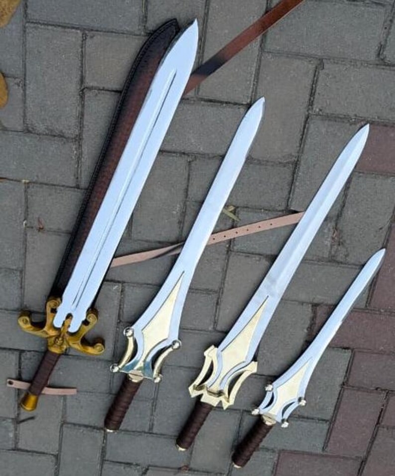 May include: Four fantasy swords with silver blades and gold and brown handles are displayed. One sword is in a brown sheath. The swords vary in size, with ornate gold detailing on the handles. The swords are arranged on a brick surface.