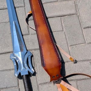 Pu&ograve; includere: Una spada d'argento con un'elsa decorativa e un'impugnatura avvolta in nero &egrave; appoggiata accanto a un fodero in pelle marrone con una tracolla. La spada ha una lama appuntita e un pomo d'argento.