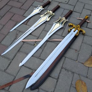 May include: Four swords with polished steel blades and ornate gold-colored hilts. The handles are wrapped in brown leather. One sword is sheathed in a brown leather scabbard. The swords are arranged on a gray brick surface.