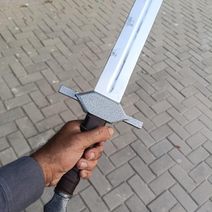 May include: A silver and gray sword with a brown handle. The blade is long and shiny, and the handle has a textured grip. The sword has a crossguard and a pommel. The sword is held in a hand.