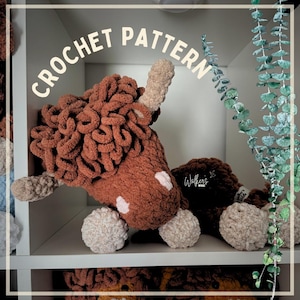 May include: A plush highland cow toy made of brown and beige yarn with a curly texture, featuring the text CROCHET PATTERN at the top. The toy has light beige horns and hooves, with a small white patch on its face and a Walker's Wilds logo tag.
