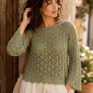 Può includere: Un top a maniche lunghe all'uncinetto color verde salvia con un delicato motivo floreale, un ampio scollo a barchetta e bordi smerlati sulle maniche e sull'orlo. Il capo è abbinato a pantaloni beige chiaro e una borsa a tracolla intrecciata.