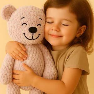 Könnte beinhalten: Ein helllila gehäkelter Teddybär mit einem lächelnden Gesicht wird umarmt. Der Bär hat eine schwarze Nase und einen schwarzen Mund sowie schwarz genähte Augen. Der Bär ist aus weichem, strukturiertem Garn gefertigt. Das Kind trägt ein beiges T-Shirt.