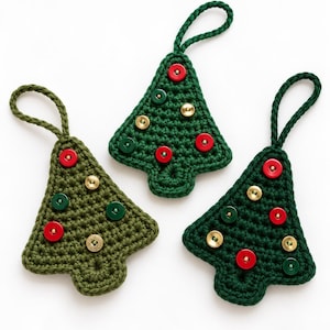 Pode incluir: Três enfeites de árvore de Natal em crochê com fios em vários tons de verde. Cada árvore tem uma alça no topo para pendurar e é decorada com pequenos botões redondos e planos nas cores vermelho, verde escuro e dourado metálico.