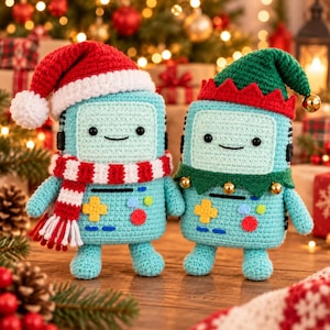 May include: Two light blue crochet plush toys shaped like handheld game consoles. One wears a red and white Santa hat and a matching striped scarf. The other wears a green elf hat with a red jagged brim and small gold jingle bells attached.