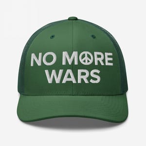 Op de afbeelding: Een groene truckerpet met de witte geborduurde tekst "NO MORE WARS". Het vredesteken vervangt de "O" in "MORE". De pet heeft een mesh achterkant en een gebogen klep.