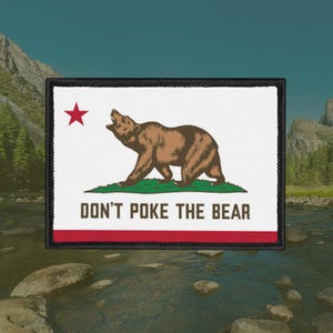 Puede incluir: Parche rectangular con el diseño de la bandera del estado de California. Presenta un oso pardo, una estrella roja y el texto "DON'T POKE THE BEAR" sobre un fondo blanco, con un borde rojo y costuras negras.
