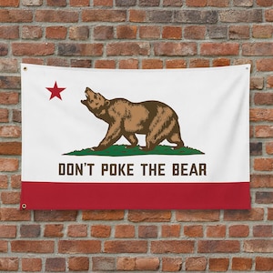 May include: A white flag with the California state flag design. It features a brown bear, a red star, and the text "DON'T POKE THE BEAR" in black. The bottom stripe is red.