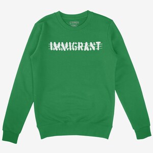 Op de afbeelding: Een groene sweatshirt met het woord "IMMIGRANT" in witte, vervaagde letters over de borst. De sweatshirt heeft een ronde hals en lange mouwen. De merknaam "STERNE GANG" staat boven het woord "IMMIGRANT" gedrukt.