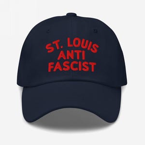 Navy blue dad hat with “St. Louis Anti Fascist” in bold red embroidery, showing contrast customization.
