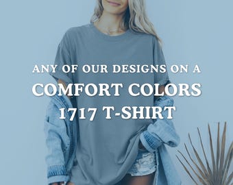 Puede incluir: Una persona con una camiseta gris Comfort Colors 1717. La camiseta tiene el texto blanco "ANY OF OUR DESIGNS ON A COMFORT COLORS 1717 T-SHIRT". La persona también lleva una chaqueta vaquera y pantalones cortos.