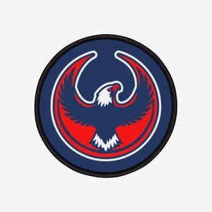 Può includere: Toppa rotonda con un'aquila stilizzata con le ali spiegate. L'aquila è principalmente blu navy con accenti rossi e bianchi. La toppa ha un bordo nero ed è probabilmente progettata per essere cucita o stirata sul tessuto.