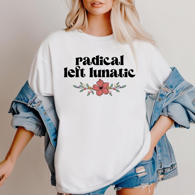 以下が含まれることがあります： 黒のスタイリッシュなフォントで「radical left lunatic」というテキストがプリントされた白いTシャツ。テキストの下には、赤い花と緑の葉のフローラルデザインがあります。Tシャツはデニムジャケットと合わせて着用されています。