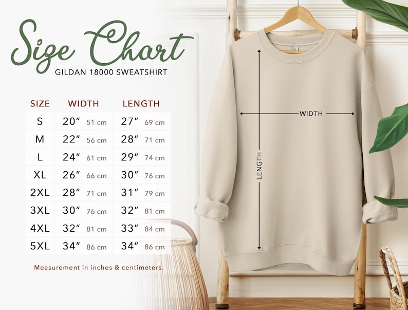 Puede incluir: Una sudadera beige Gildan 18000 cuelga de un estante de madera, con medidas de ancho y largo. Una tabla de tallas muestra las tallas S a 5XL, con medidas en pulgadas y cent&iacute;metros. La tabla incluye un ancho de 51 cm a 86 cm y un largo de 69 cm a 86 cm.