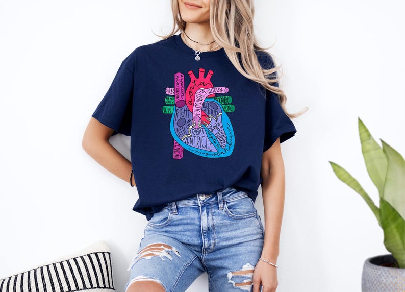 Puede incluir: Camiseta azul marino con una colorida ilustraci&oacute;n de un coraz&oacute;n anat&oacute;mico. El dise&ntilde;o del coraz&oacute;n incluye partes etiquetadas en varios colores, como rosa, azul y verde. Una prenda de vestir informal.