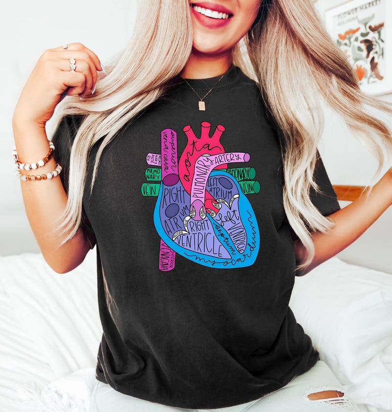 Puede incluir: Camiseta negra con un colorido diagrama anat&oacute;mico del coraz&oacute;n con partes etiquetadas como aorta, aur&iacute;cula y ventr&iacute;culo. El dise&ntilde;o incluye tonos de rosa, azul y morado, con el texto en blanco. Una camiseta gr&aacute;fica casual y educativa.