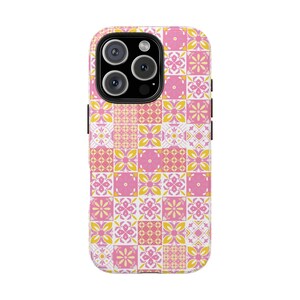 Pode incluir: Uma capa de telefone com um padrão de azulejos rosa, amarelo e branco. A capa tem um design quadrado com um padrão repetitivo de formas florais e geométricas. A capa do telefone tem um módulo de câmera preto com três lentes.