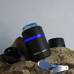 May include: Black insulated container with a blue stripe and the text "ARCTIC ZONE". The container has a silver lid and a black lid. A silver spoon is next to the container. The container is on a rocky surface.