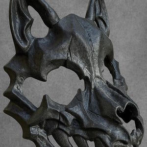 May include: A dark grey wolf skull mask with sharp teeth and pointed ears. The mask has a textured surface and is held up by a hand. The mask is likely for cosplay or costume use.