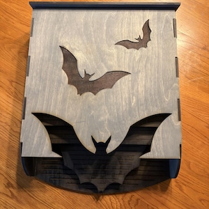 May include: A wooden box with a gray finish and bat cutouts. The box features three bat silhouettes, with a large bat design at the bottom. The box is made of wood and has a dark gray trim.