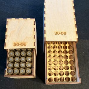 May include: Two light-coloured wooden storage boxes with finger-jointed edges. The smaller box is filled with brass-coloured 30-06 cartridges. The larger box is empty, featuring a grid of circular cutouts for storage. Both boxes are labelled 30-06.
