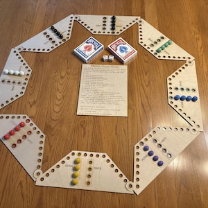 Peut inclure: Un jeu de Marble Chase en bois avec des billes multicolores, deux jeux de cartes à jouer Bicycle et des dés. Le plateau de jeu est composé de pièces en bois imbriquées. Une feuille de papier avec les règles du jeu est au centre.