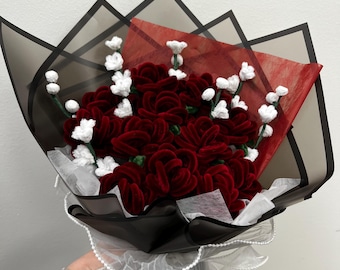 May include: A bouquet of deep red velvet roses and white floral accents, wrapped in black and red paper with a white ribbon. The bouquet is a handmade floral arrangement.