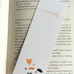 May include: White bookmark with the name "NORRIS" and the number "4" in orange. The bookmark features small orange and black racing-themed graphics, including a heart, stars, and a race car.