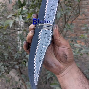 May include: A black and silver knife with the word "Blade" in blue text. The knife has a patterned design along the spine and a dark blade. The text "Knife Domestic" is also visible.