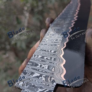 Pode incluir: Close-up de uma l&acirc;mina de faca de a&ccedil;o Damasco. A l&acirc;mina tem um acabamento escuro, quase preto, com um design ondulado. A borda tem um detalhe em cor de cobre. O texto "Blade Knife Domestic" &eacute; vis&iacute;vel.