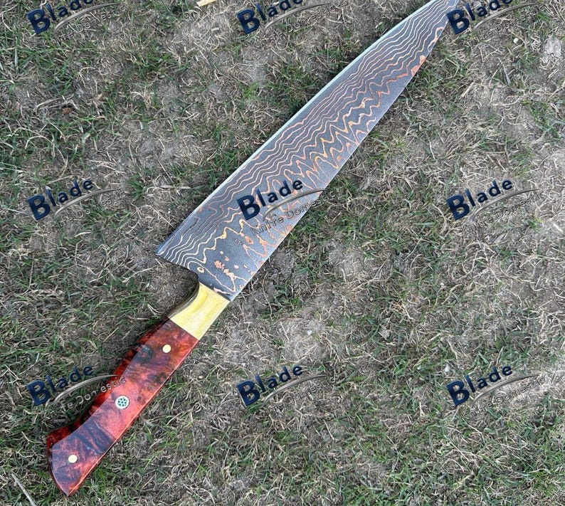 May include: A large chef's knife with a patterned blade and a wooden handle. The blade has a wavy design in shades of brown and gold. The handle is a mix of red and brown wood with brass accents.