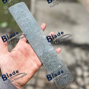 May include: A rectangular, gray knife sharpening steel with a patterned surface. The text "Blade Knife Domestic" is printed on the image. The steel is held in a hand.