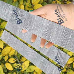 May include: Three gray, textured metal blades with the word "Blade" printed on them. The blades are held over a bed of yellow and green leaves. The blades have a unique pattern.