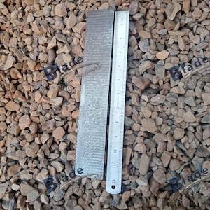 May include: A rectangular piece of patterned metal next to a ruler. The metal has a textured surface with a repeating pattern. The ruler shows measurements in inches, with the metal piece measuring approximately 12 inches in length.