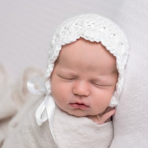 May include: A sleeping newborn baby wearing a white crocheted bonnet with a white satin ribbon tied under the chin.