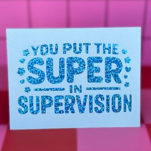 May include: A white rectangular greeting card featuring the blue glitter text "YOU PUT THE SUPER IN SUPERVISION" with small blue glitter flower and heart icons surrounding the word "SUPER" on the front of the card.