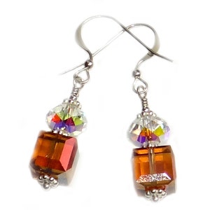 May include: A pair of silver dangle earrings with a clear crystal and a brown square crystal.