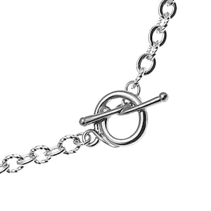 May include: Silver chain necklace with a toggle clasp. The chain is made of small, linked circles.