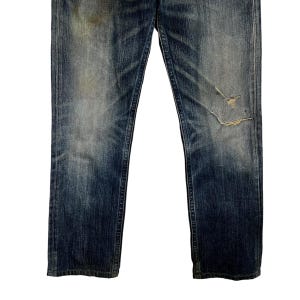 May include: Faded blue denim jeans with distressed details, including a tear on the right knee. The jeans have a classic five-pocket design and a straight leg cut. The denim shows signs of wear and fading.