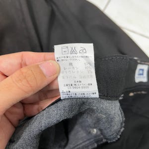 May include: Close-up of a black garment with a tag. The tag displays Japanese text, care symbols, and fabric composition: 57% cotton, 40% rayon, and 3% polyurethane. The tag also includes a warning about color transfer.