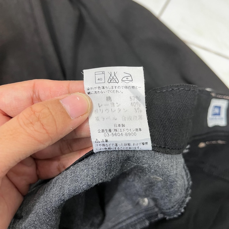 May include: Close-up of a black garment with a tag. The tag displays Japanese text, care symbols, and fabric composition: 57% cotton, 40% rayon, and 3% polyurethane. The tag also includes a warning about color transfer.