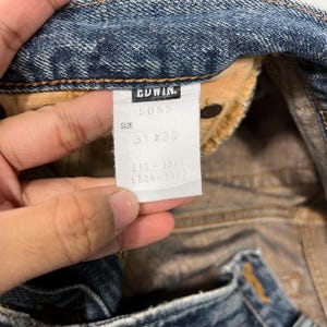 May include: A white tag with black text that reads "EDWIN", "5053", "SIZE 31 x 33", "EKS - 1301", "E506 - 1301".