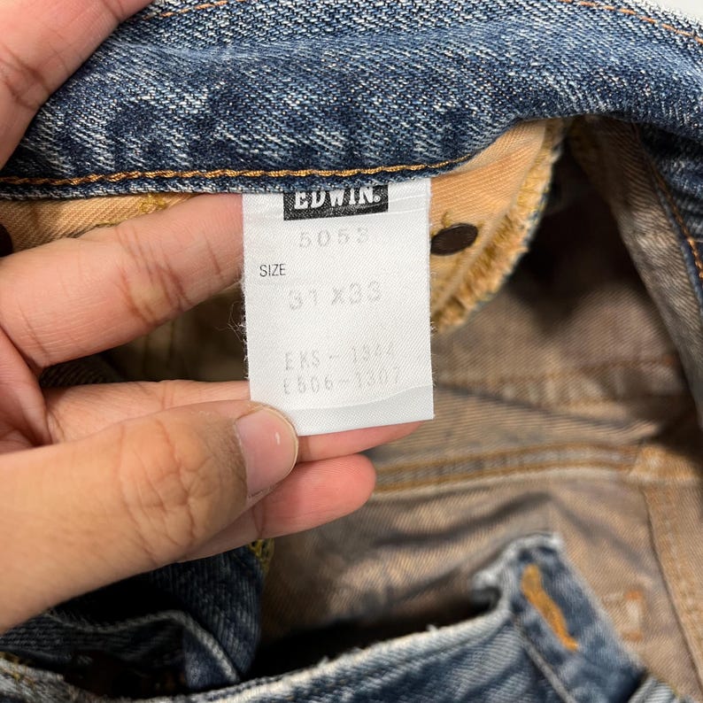 May include: A white tag with black text that reads "EDWIN", "5053", "SIZE 31 x 33", "EKS - 1301", "E506 - 1301".