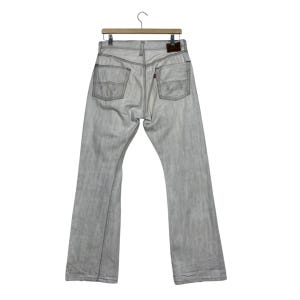 May include: Light gray denim jeans hanging on a wooden hanger. The jeans have a faded appearance with visible stitching and pockets. A small brown leather patch is visible on the back. The jeans are a classic style.